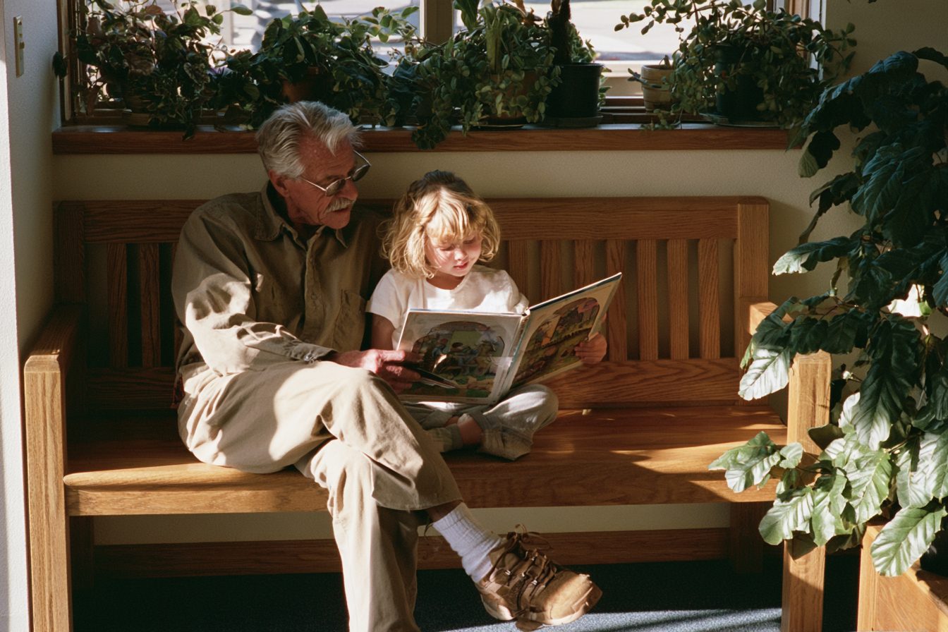A grandfather and granddaughter reading together in a sunny waiting room